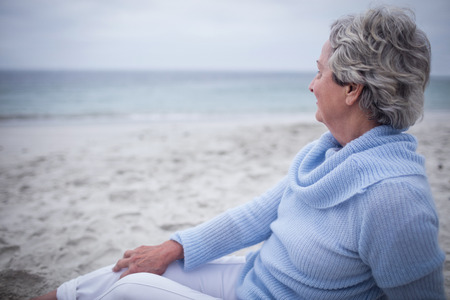 Thoughtful senior woman sitting on beach on a sunny dayの写真素材