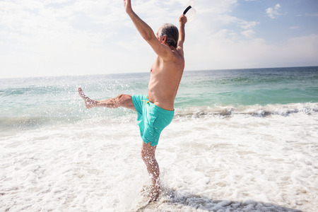 Happy senior man splashing water with her feet on the beachの写真素材