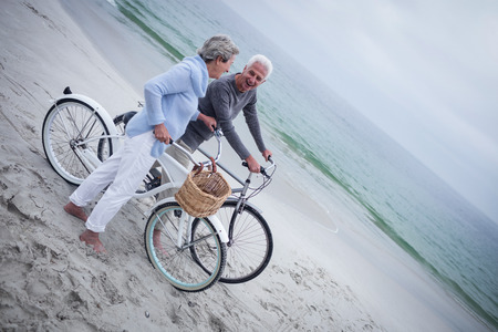 Senior couple having ride with their bike on the beachの写真素材