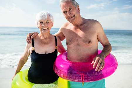 Portrait of senior couple in inflatable ring standing on beachの写真素材