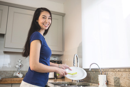 Portrait of happy woman washing up in the kitchen at homeの写真素材