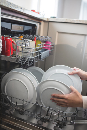 Woman in kitchen arranging plates in dish washerの写真素材