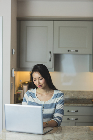 Young woman using a laptop in the kitchen at homeの写真素材