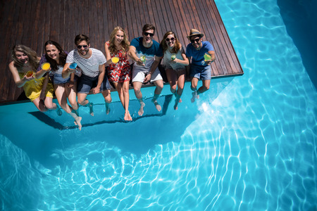 Happy friends with cocktail glass sitting side by side in swimming poolの写真素材