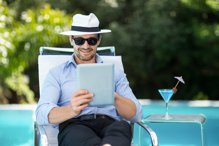 Smart man relaxing on sun lounger and using a digital tablet near the poolの写真素材