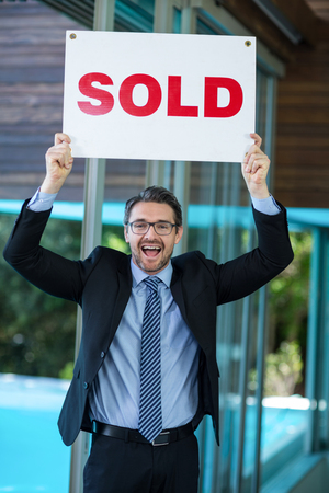 Excited real estate agent holding sold sign at resortの写真素材