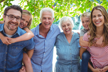Portrait of smiling family with grandparents standing against treeの写真素材