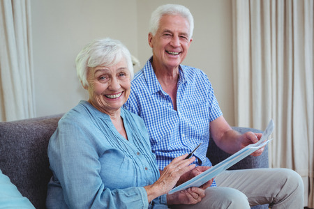 Portrait of smiling senior couple with bills while sitting on sofa at homeの写真素材