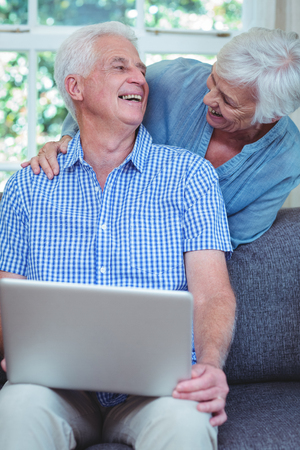 Smiling retired couple using laptop at homeの写真素材