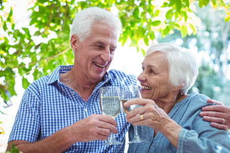 Retired couple toasting white wine while sitting at tableの写真素材