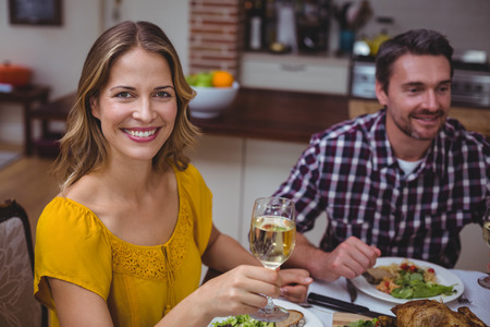 Portrait of smiling woman holding white wine while sitting at dining table