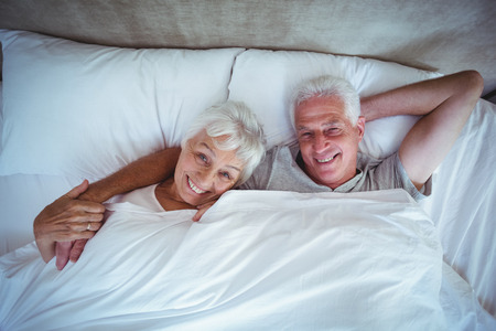 Portrait of happy senior couple lying on bed in roomの写真素材
