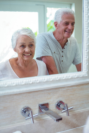Happy senior couple reflecting on mirror in bathroomの写真素材