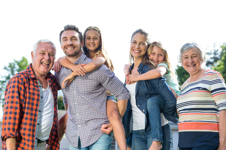Portrait of happy parents carrying girls with grandparents standing in back yardの写真素材