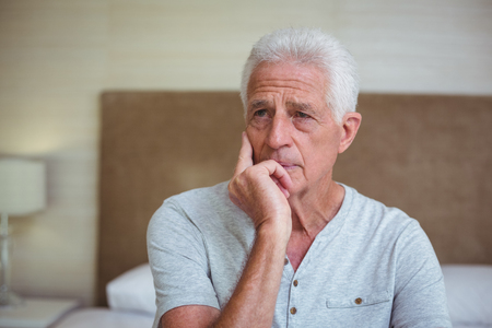 Thoughtful senior man sitting on bed in roomの写真素材