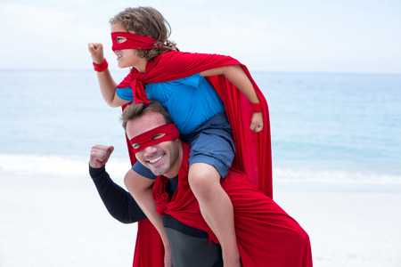 Happy father and son in superhero costume pretending to run at beachの写真素材