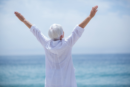 Rear view of senior woman exercising at beach on sunny dayの写真素材