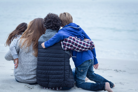 Rear view of family sitting on sea shore at beachの写真素材