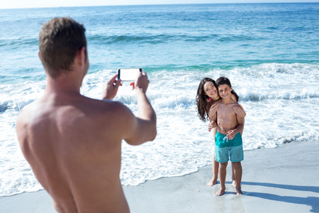 Father photographing happy wife and son at sea shoreの写真素材