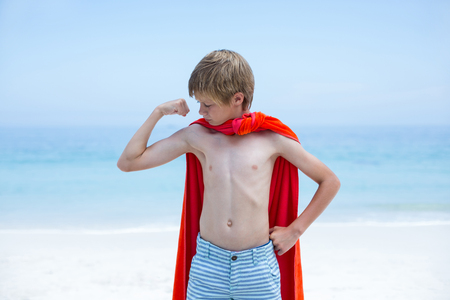 Shirtless boy in superhero costume flexing muscles at beachの写真素材