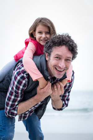 Portrait of happy father carrying daughter on back at sea shoreの写真素材