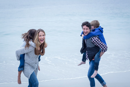 Cheerful parents enjoying while carrying children on back at sea shoreの写真素材