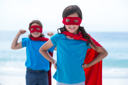 Portrait of happy siblings in superhero costume standing at sea shoreの写真素材