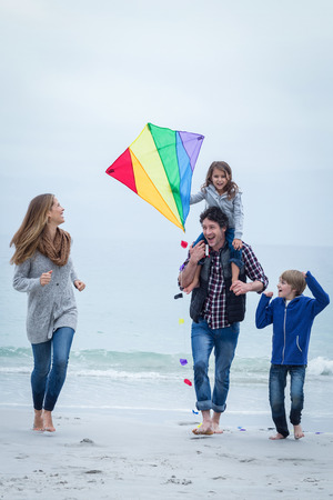 Full length of happy family with kite enjoying at sea shoreの写真素材