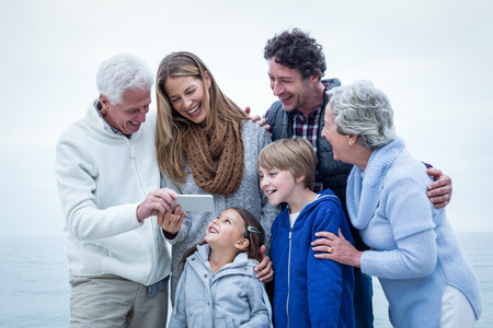 Happy family looking in phone at beach against skyの写真素材