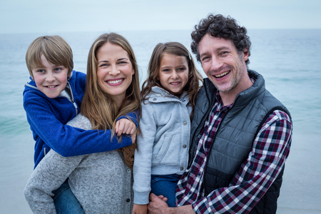 Portrait of parents smiling while carrying children at sea shoreの写真素材