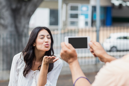 Man photographing woman blowing kiss in cityの写真素材
