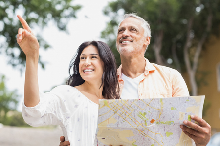 Happy woman pointing away while man holding map in cityの写真素材