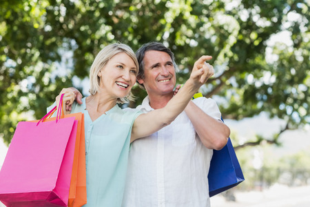 Woman pointing to happy man with shopping bags against treesの写真素材