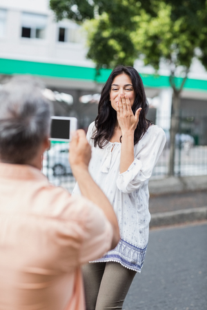Rear view of man photographing happy woman blowing kiss in cityの写真素材