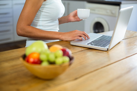 Fruits in bowl on table with woman working on laptop at homeの写真素材