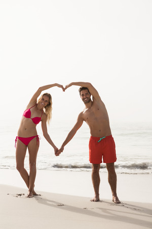 Couple forming a heart with arms on the beachの写真素材