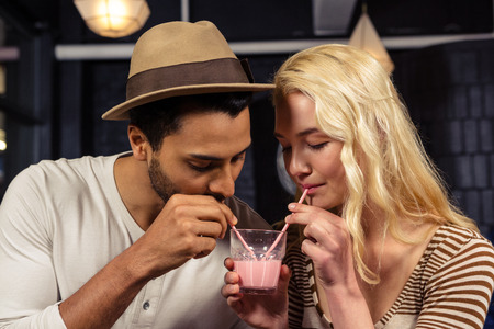 Couple sharing a milkshake in a coffee shopの写真素材