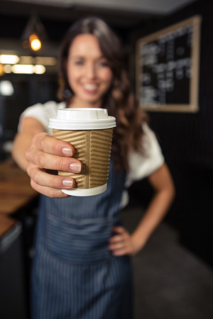 Smiling barista holding disposable cup at coffee shopの写真素材