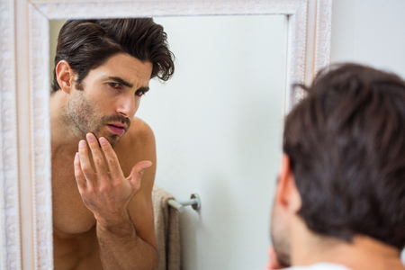 Man looking in mirror and checking his stubble in bathroomの写真素材