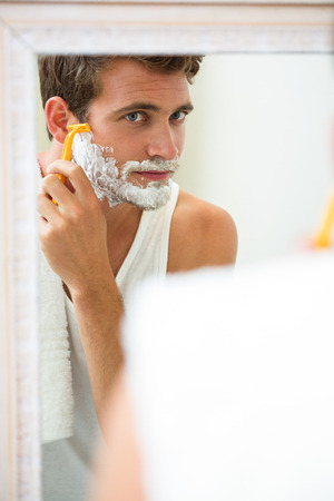 Young man shaving in front of bathroom mirrorの写真素材