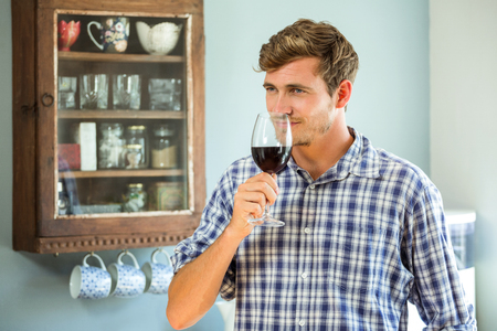 Young man smelling a glass of red wine in kitchenの写真素材