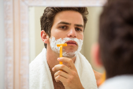 Young man shaving in front of bathroom mirrorの写真素材