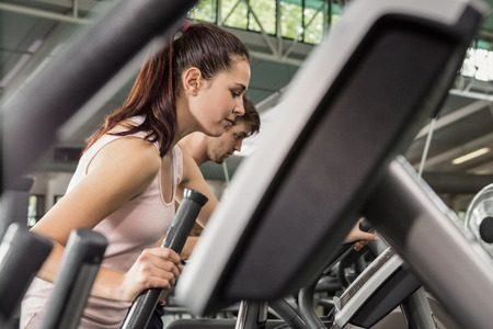 Beautiful woman and man exercising on the elliptical machine at gymの写真素材