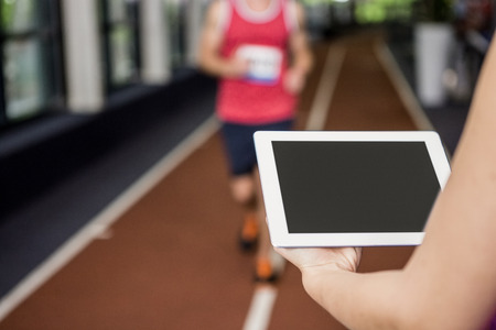 Trainer using a digital tablet while man performing running exercise in gym