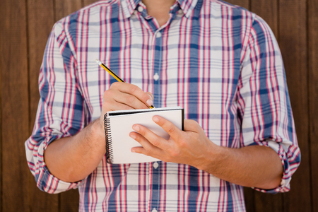 Mid section of man writing in a diary on a wooden backgroundの写真素材