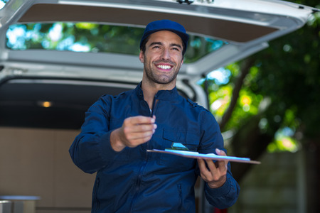 Smiling delivery person giving clipboard for signature while standing by vanの写真素材