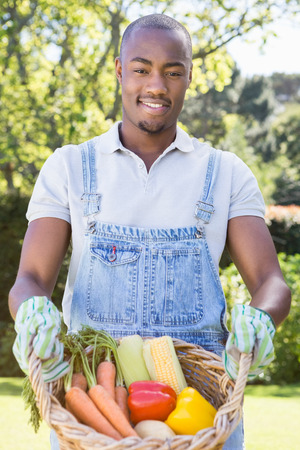 Portrait of young man holding a basket of freshly harvested vegetables in gardenの写真素材