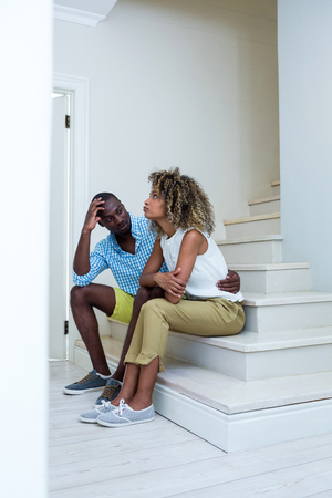 Young couple at home sitting on steps and talkingの写真素材