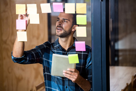 Man using digital tablet while writing on sticky notes in office