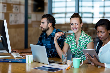 Young man and women sitting at their desk and using laptop, digital tablet and personal computer in the officeの写真素材
